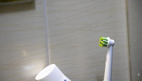 A close-up of an electric toothbrush and toothpaste tube on a tiled bathroom Foto stock
