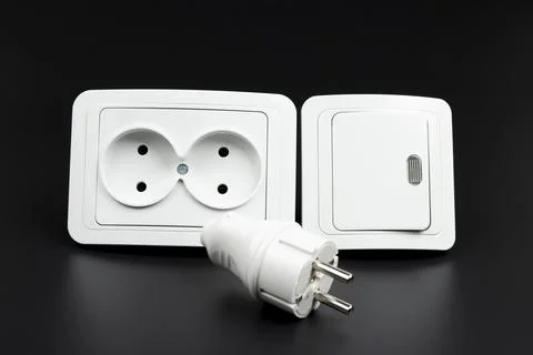 Close-up of electrical outlet, plug and light switch on black background Foto stock