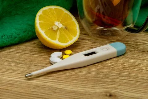 Close-up of an electronic thermometer, half a lemon, and flu medication Stock Photos