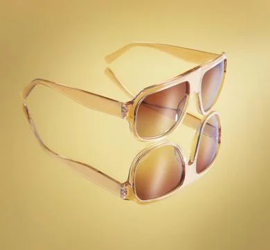 Close up of elegant amber translucent sunglasses reflecting on a golden bac.. Stock Photos