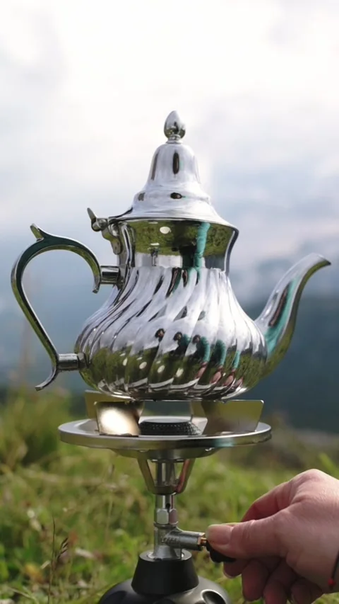 Close-up of elegant silver teapot on portable stove with blurred mountains in Stock Footage 319506272