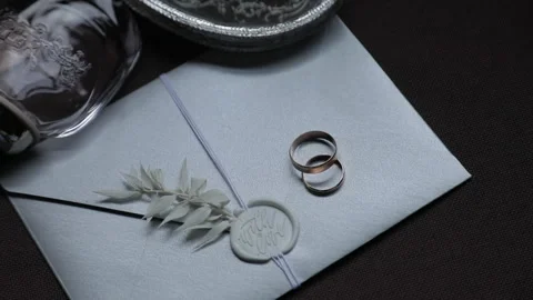 A close-up of an elegant wedding invitation with wedding rings placed on it Stock Footage 322558567