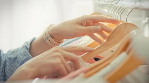 A close-up of elegant well-groomed hands browsing clothes on wooden hangers Stock Footage 341490875