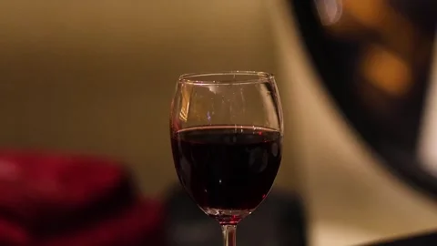 Close up of elegant wine glass filled with red wine against blurry evening .. Vídeos de archivo 333486747