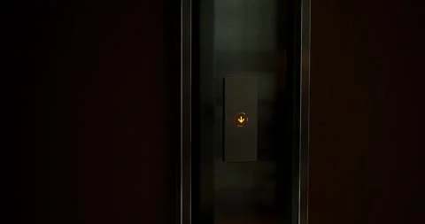 A close-up of the elevator call button which glows yellow and shows a down arrow Vídeos de archivo 283542297