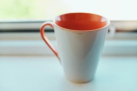 Close-up of empty ceramic coffee mug with orange interior resting on white .. Stock Photos