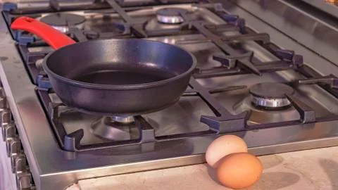 Close-up empty frying pan with red handle on the stove. Next are two chicken  Photos