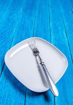 Close-up of empty squared white ceramic plate and silver cutlery on blue wooden Stock Photos