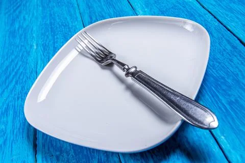 Close-up of empty squared white ceramic plate and silver cutlery on blue wooden Stock Photos