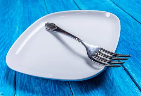 Close-up of empty squared white ceramic plate and silver cutlery on blue wooden Stock Photos