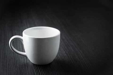 Close up empty white coffee cup on black wood table near window with light sh Stock Photos