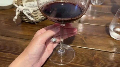 Close up of engagement ring hand holding red wine glass in cozy setting Stock Footage 319691876