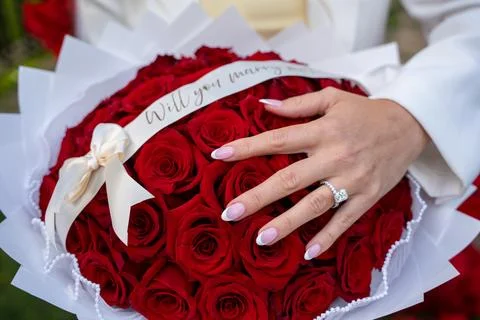 Close up of engagement ring on hand with red rose bouquet Stock Photos