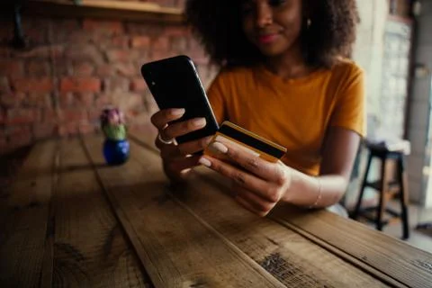 Close up of ethnic customer making payment with card texting friends off Stock Photos