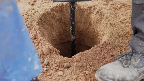 Close-up excavation site with deep sandy hole, black digging tool centered, blue Vidéo 344873006