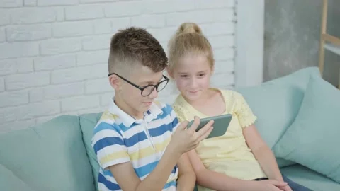Close up of an excited twins kids using smartphone sitting together on sofa Stock Footage 168976945