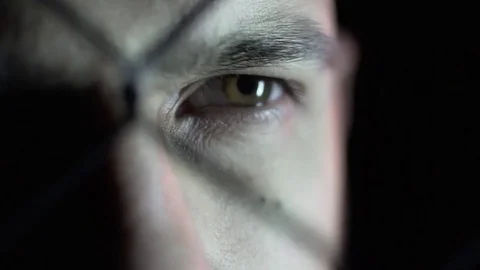 Close-up of an eye of a man behind a grid. It's a dark room. Stock Footage 80862212
