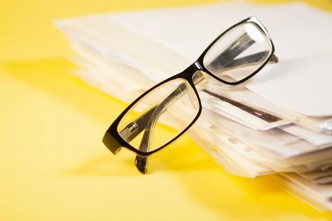 Close up of eyeglasses and stack of papers on yellow background Stock Photos