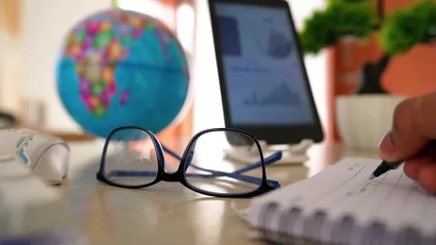 Close-up of eyeglasses on a desk with a globe, tablet, and notebook Stockbeeldmateriaal 320724866