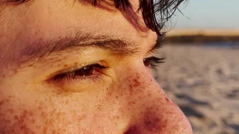 Close up of the eyes of a freckled young man looking at the sea at sunset Stock Footage 304662653