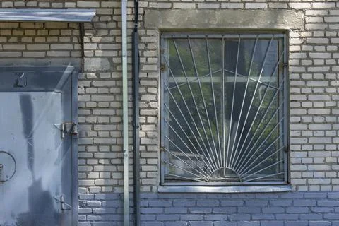 Close-up of the facade of an old brick building with a barred window and a me Stock Photos
