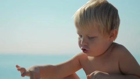 Close-up of the face of a 5 year old blond boy playing with rocks on the beach Stock Footage 229277211