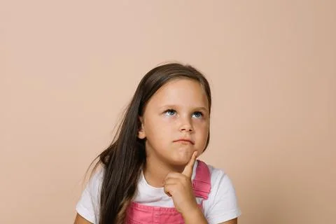 Close-up face kid with shining bright eyes looking upward, point finger on chin Stock Photos