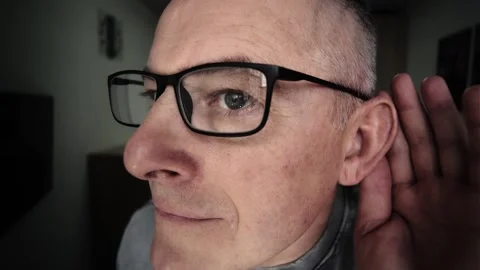 A close-up of the face of a man with glasses, putting his hand to his ear trying Stock Footage 315339174
