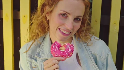 Close up of face red curly haired young woman smiling after eating pink donut Stock Footage 160549384
