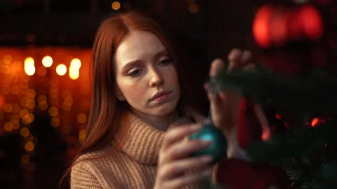 Close-up face of sad redhead young woman decorating Christmas tree alone at cozy Stock Footage 143955302