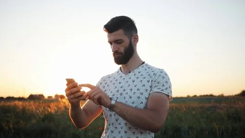 Close up face serious young attractive bearded man with use phone in field Stock Footage 92064905