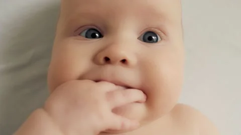 Close up face with soft tender skin of cute child lying on bed chewing fingers Stock Footage 169390731
