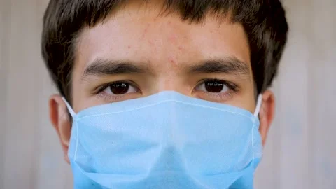 Close up of the face of young man wearing a blue medical mask and looking at the Vídeos de archivo 137504729