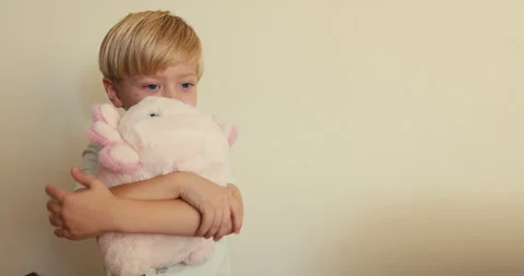 A close-up of a fair-haired, blue-eyed boy hugging his soft pink Axolotl and Video stock 346982842