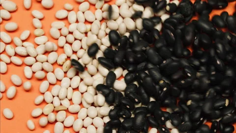 Close-up of falling down black beans on glass table from jar on yellow Stock Footage 155126721