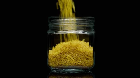 Close-up of falling down bulgur into glass jar on black background. Shooting of Stock-Footage 155171280