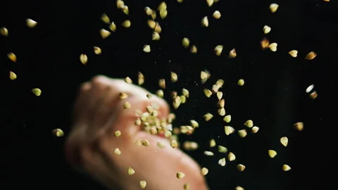Close-up of falling down green buckwheat from the fist of hand on glass table on Stock Footage 155127091