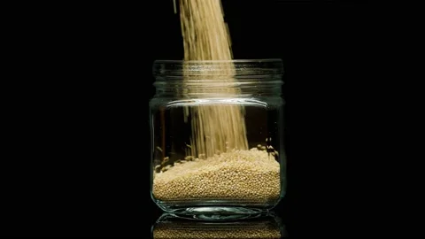 Close-up of falling down quinoa into glass jar on black background. Shooting of Stock Footage 156007682
