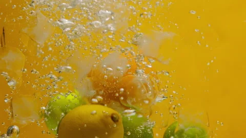 Close-up of falling limes, oranges and lemons into the water with ice on orange Stock Footage 156007693