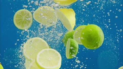 Close-up of falling ripe limes and lemons into sparkling water on blue Stock Footage 158678890