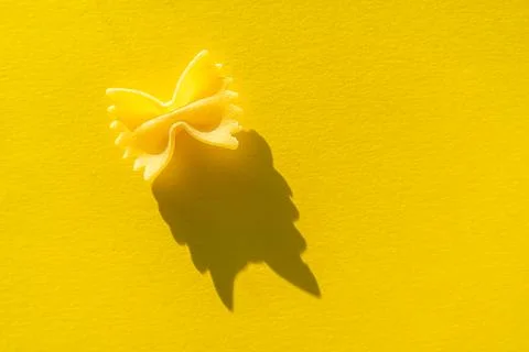 Close-up of farfalle paste on a yellow background in bright light Stock Photos