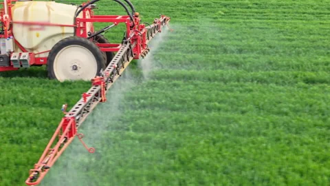 Close-up of a farmer spraying crop field with red machinery sprayer. Aerial Stock Footage 310035922