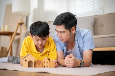 Close up of father looking at elementary son playing with wooden house toy .. Stock Photos
