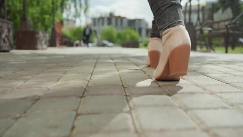 Close up of feet in beige high heel boots walking on cobblestone pavement with Stock Footage 345047294