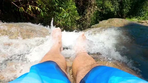 Close-up of feet dangling over crystal clear water of waterfall Stock Footage 168706443