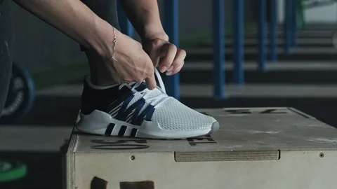 Close-up of feet of female runner getting ready tying running shoes in gym Stock Footage