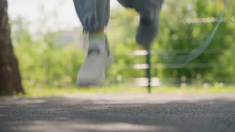 Close up of feet jumping blue skip rope on asphalt path with green foliage Vidéo 345843603