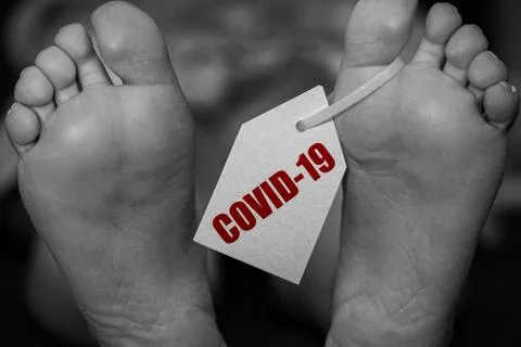 Close up feets of corpse in morgue on table tagged with the inscription COVID-19 Stock Photos
