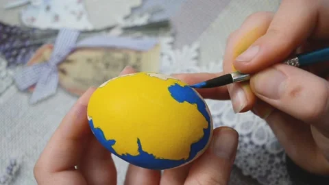 Close-up female arms painting Easter egg into flag of Ukraine colors in shape of Stock Footage 178039668