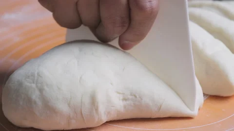 Close-up of female baker cutting dough on portion with kitchen utensil on table. Stock-Footage 167781752